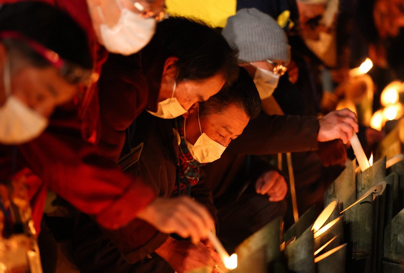 阪神大震災から27年。「1・17のつどい」で竹灯籠(とうろう)に灯をともす人たち=神戸市中央区の東遊園地で2022年1月17日午前5時11分、猪飼健史撮影