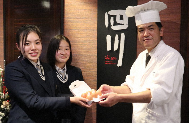 料理長(右)に、パック詰めされた「玄米タマゴ」を手渡す京都府立農芸高校の生徒=京都市内で、小栁津早霧撮影