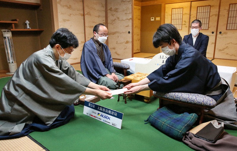 第71期ALSOK杯王将戦七番勝負第2局で、立会の谷川浩司九段(左)に封じ手を渡す挑戦者の藤井聡太竜王(右)。左奥は渡辺明王将=大阪府高槻市の山水館で2022年1月22日午後6時29分、大西達也撮影