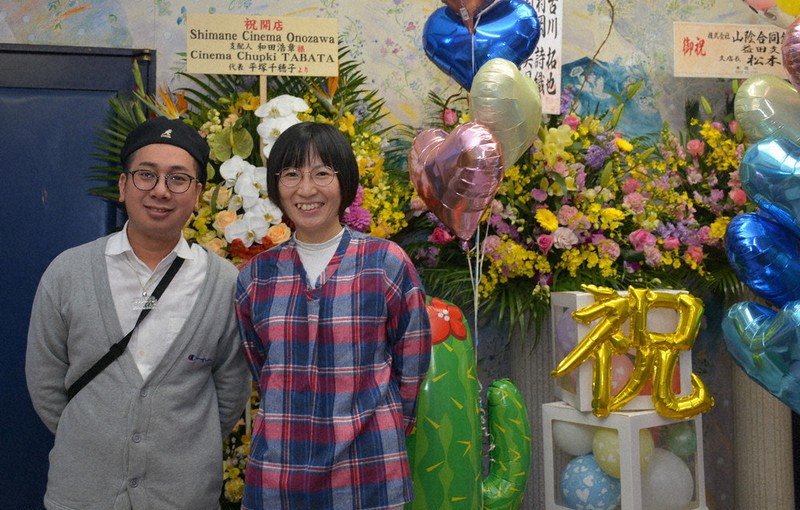 映画館の復活オープンを祝う花に囲まれる和田浩章さん(左)と更沙さん=島根県益田市で、萱原健一撮影