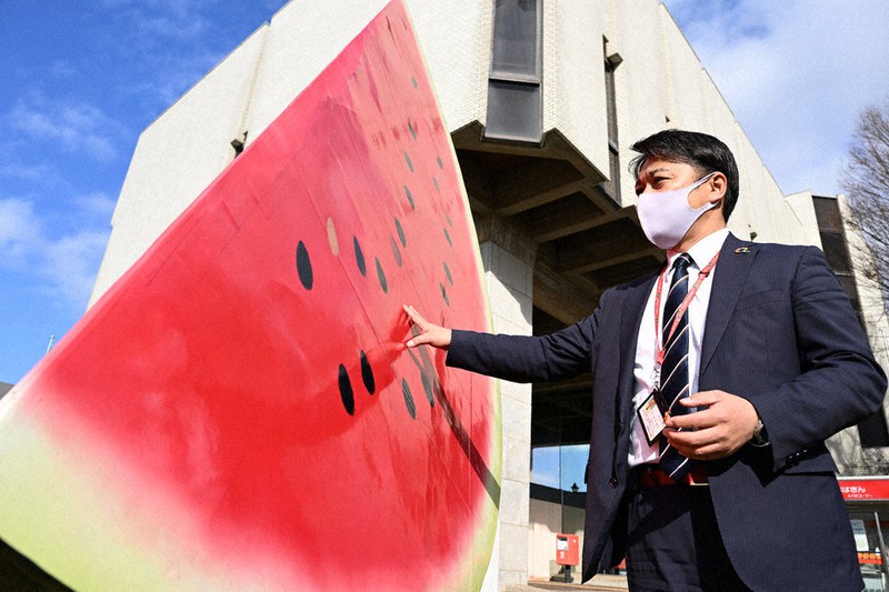 巨大なスイカのモニュメントに手を当てる、千葉県富里市の永田健矢企画課長。返礼品競争に苦戦し、ふるさと納税による収支は赤字だ=富里市役所で2021年12月9日、宮間俊樹撮影