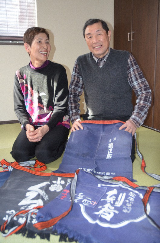 店に出るときに身につけていた前掛けを手に、当時を振り返る「中村屋酒店」店主だった中村光雄さん(右)と妻元江さん=北区赤羽西で