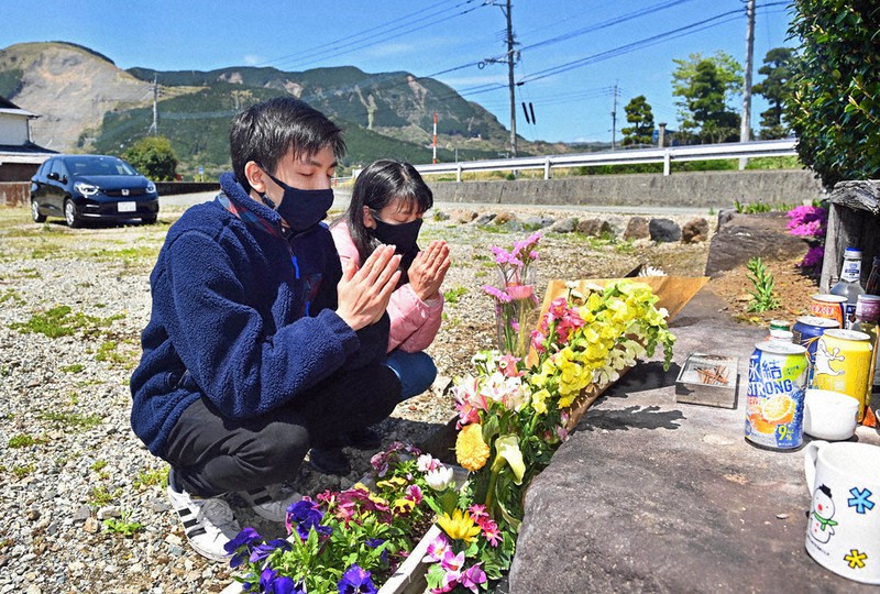 熊本地震の本震から6年。東海大生の大野睦さん(当時20歳)が亡くなったアパート跡地で、手を合わせる後輩の茨木信人さん(左)、母洋美さん親子。信人さんは「6年がたち復興で村の姿は変わりつつあるが、大野さんのことを忘れていない人はたくさんいる。先輩の分まで一生懸命生きます」と話した。左後方は当時、大規模に崩落した斜面=熊本県南阿蘇村で2022年4月16日午後0時18分、平川義之撮影