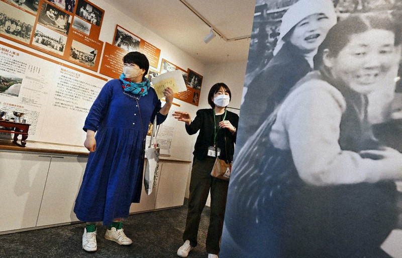 常設展示場で、スタッフ(右)の説明を聞きながら見学する来館者=京都府宇治市で2022年4月30日午前11時52分、山崎一輝撮影