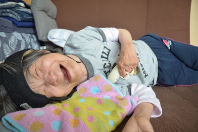 自宅の床に寝そべり、笑ったような表情を見せる田中実子さん＝熊本県水俣市で2022年5月1日午前10時29分、西貴晴撮影