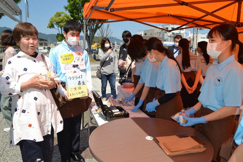 伊万里駅前公園でスイーツを購入した女性(左端)に募金を呼びかけるフードプロジェクト部員(左から2人目)ら