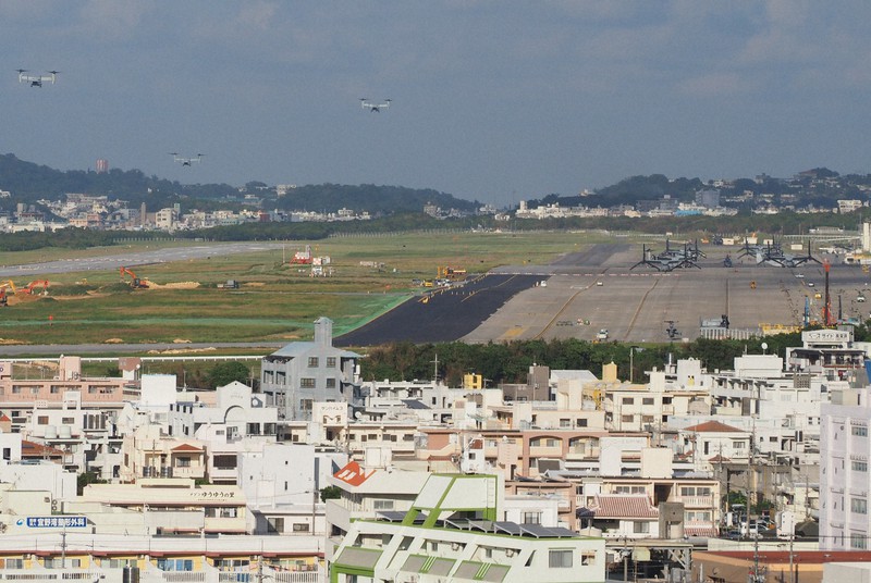 市街地に囲まれた米軍普天間飛行場。左上をオスプレイが飛んでいる=宜野湾市嘉数1の嘉数高台公園で2017年11月2日午後4時22分、鈴木英生撮影