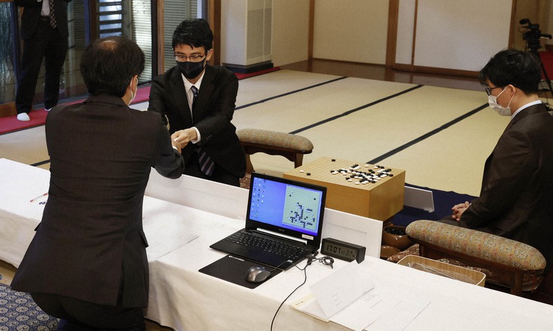 第77期本因坊戦第1局で封じ手を立会人の羽根直樹九段に渡す挑戦者の一力遼棋聖(中央)。右は本因坊文裕=金沢市の金渓閣で2022年5月10日午後5時7分、三村政司撮影