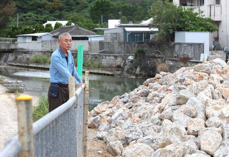 沖縄振興予算の減額により川の整備が進まず、積み上げられたままになっている護岸用の岩の山を見つめる崎浜秀雄さん=沖縄県名護市で2022年4月27日午後4時52分、喜屋武真之介撮影