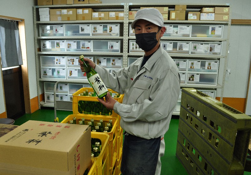 「繁桝」を手にする高橋商店の鈴木啓さん。後ろには商品のラベルを種類ごとに仕分けしたボックスがある=福岡県八女市で2022年4月22日、足立旬子撮影