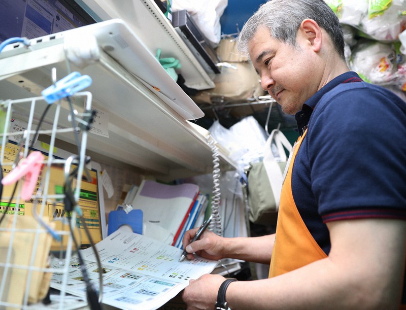 商品カタログを見つめる100円ショップ「THE 100 STORES」の宮城武志・専務=東京都目黒区で2022年4月27日午後5時34分、三浦研吾撮影