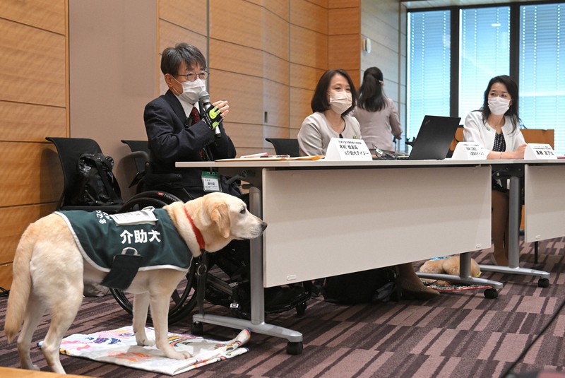 シンポジウムで話す日本介助犬使用者の会会長の木村佳友さん(左)。手前は介助犬デイジー=東京都千代田区で2022年5月20日、前田梨里子撮影