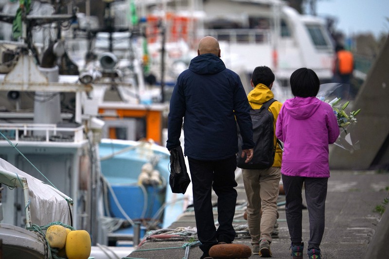 小型観光船の事故発生から1カ月となった23日、現場海域周辺に向かうため、花束を手に船に向かう地元観光船の関係者ら=北海道斜里町のウトロ漁港で2022年5月23日午前7時52分、渡部直樹撮影