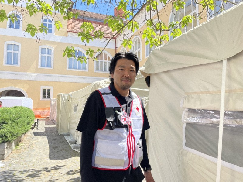 仮設診療所となるテントの前に立つ薬剤師の仲里泰太郎さん=ウクライナ西部のウジュホロドで2022年5月19日(大阪赤十字病院提供)