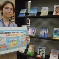 福岡県立図書館で6月末まで開設されている沖縄関連書籍コーナーを紹介する和仁屋さん＝福岡市東区で2022年6月2日午後2時19分、中里顕撮影