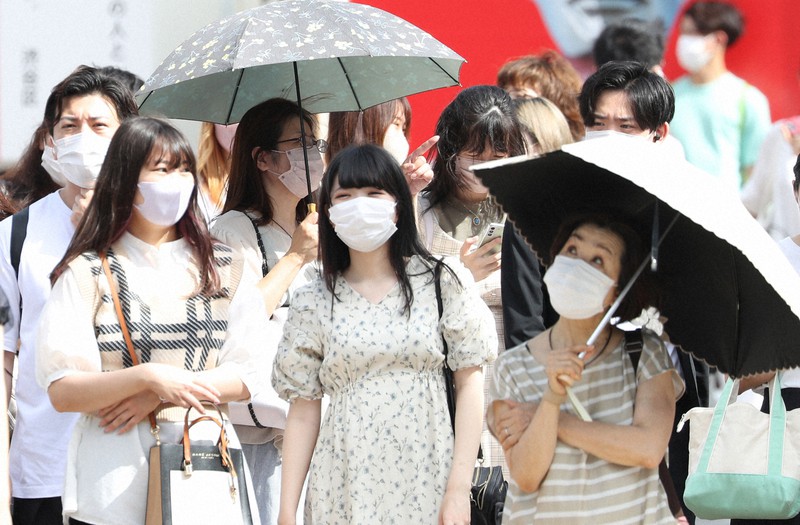 気温が上昇する中、日傘を差して信号待ちをする人たち=東京都渋谷区で2022年6月24日午後3時6分、三浦研吾撮影