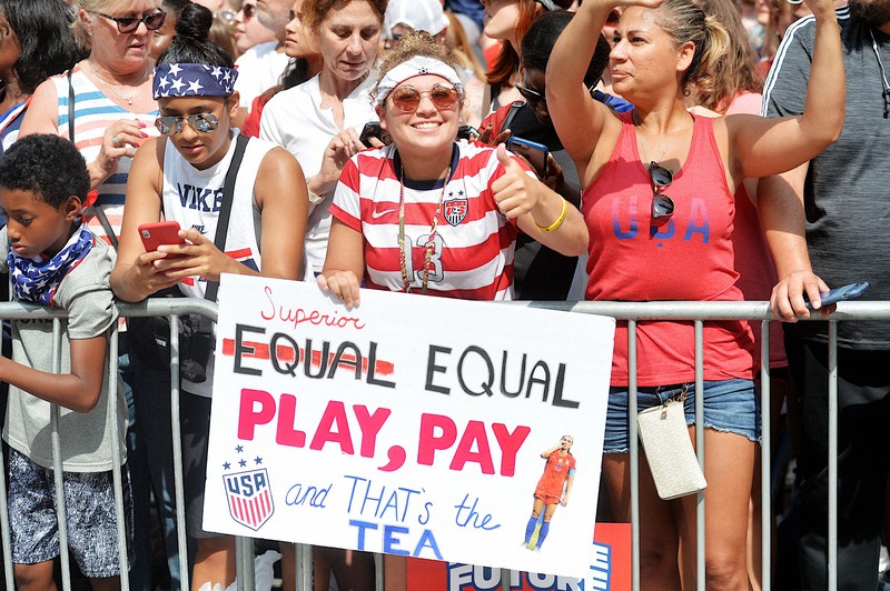 沿道で賃金の男女平等を訴えるプラカードを持つ市民=米ニューヨークで2019年7月10日、隅俊之撮影