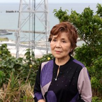 米軍ホワイトビーチ（奥）の見える高台に立つ富山光枝さん＝沖縄県うるま市で2022年6月15日、喜屋武真之介撮影