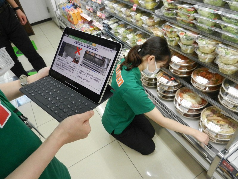 タブレット端末の「省エネアプリ」の指摘を受け、商品棚のフィルターを確認するコンビニ店員。店内は照明を間引いて営業している=東京都千代田区の「セブン-イレブン千代田二番町店」で2022年6月30日、道下寛子撮影