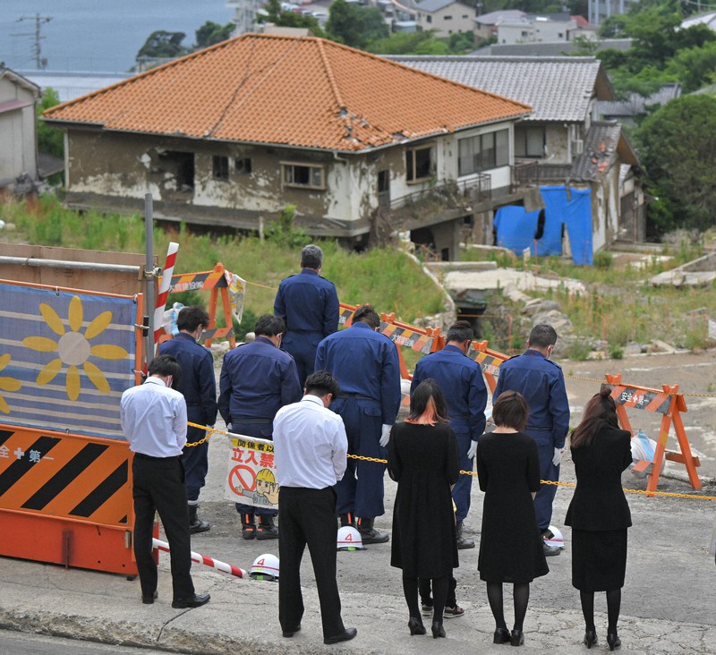 土石流災害から1年となり、土石流が流れた現場に向かって黙とうする遺族や消防関係者ら=静岡県熱海市伊豆山で2022年7月3日午前10時28分、手塚耕一郎撮影