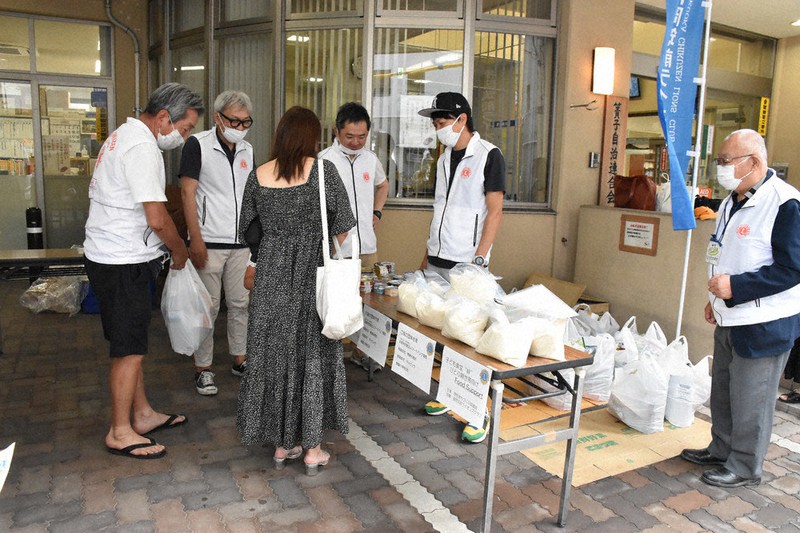 ひとり親家庭に袋いっぱいに詰めた食材を手渡す二田さん(左)
