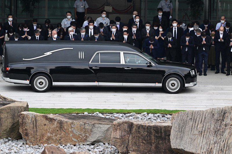 官邸前を通る安倍晋三元首相のひつぎを乗せた車に合掌する岸田文雄首相(前列左から8人目)=東京都千代田区で2022年7月12日午後3時1分、前田梨里子撮影