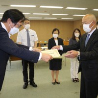 秋本・県選管委員長（左）から当選証書を受け取る、江島氏の代理人の池部・山口事務所事務局長