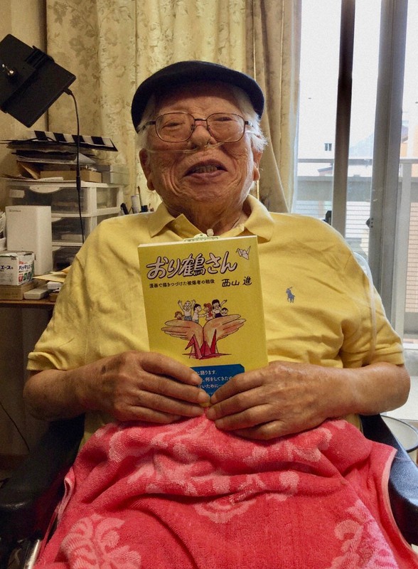 単行本になった「おり鶴さん」を手に笑顔を見せる西山進さん=「おり鶴さん」編集・出版委員会提供