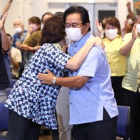 参院選沖縄選挙区で再選が確実となり、妻と抱き合う「オール沖縄」勢力の現職、伊波洋一氏（中央）＝那覇市で2022年7月11日午前0時、喜屋武真之介撮影