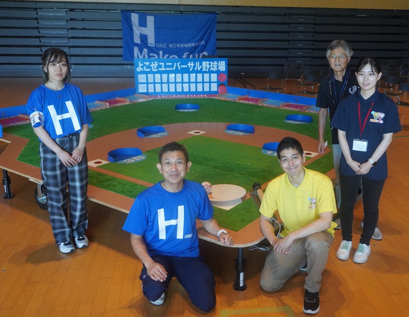 ユニバーサル野球のイベントでスタッフと「球場」を囲む中村哲郎さん(左から2人目)。「野球ゲーム盤」として堀江車輛電装が特許を取得している=茨城県つくば市で2022年7月23日午後3時24分、藤倉聡子撮影