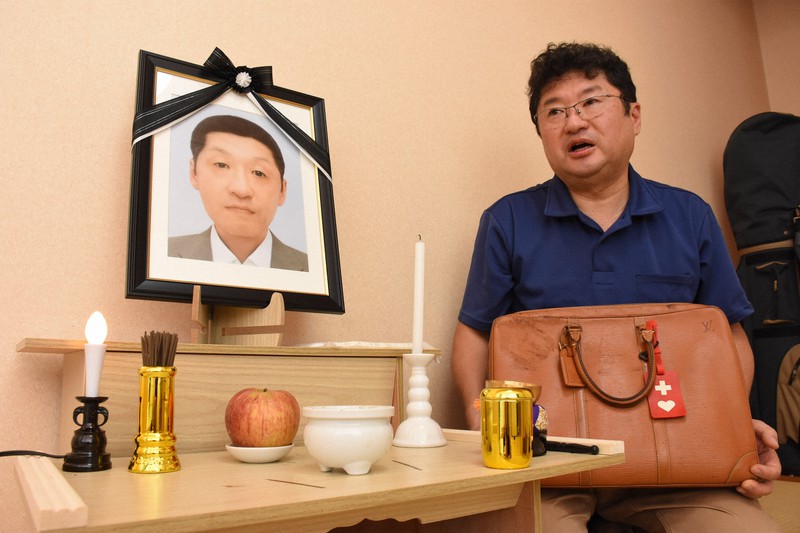 柳発秀さんの遺影を前に、兄の南秀さんは「自宅の売却は脳障害につけこんだ不当契約で無効だ」と訴えた。両手には遺品のバッグを抱えていた=大阪市生野区で2022年9月30日、郡悠介撮影