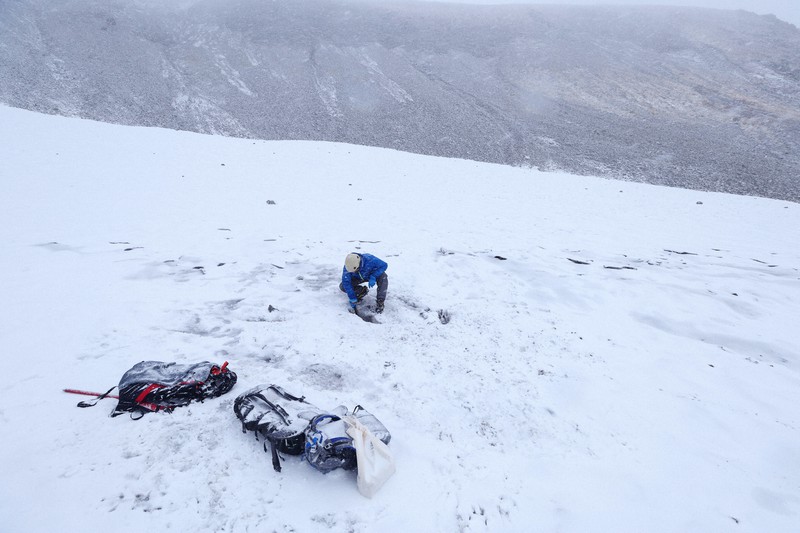 吹雪の中、内蔵助氷河でピッケルを手に雪渓に隠れる氷体を探す飯田肇さん=富山県・立山で2022年10月6日、滝川大貴撮影