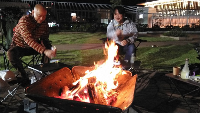 ゆらゆらと揺れるたき火の炎を見ながら酒を飲む「焚き火と日本酒ガーデン」の来場者=群馬県高崎市で2022年10月19日午後7時22分、庄司哲也撮影