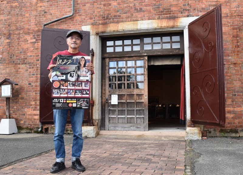 会場となる牛津赤れんが館前でジャズフェスのポスターを手にする田中さん=2022年10月7日、斎藤毅撮影