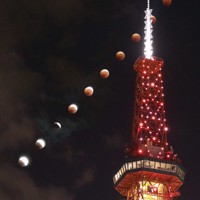 さっぽろテレビ塔の奥で部分月食から皆既月食へと進む満月（午後6時45分から6分間で撮影した10枚を合成）。札幌では午後7時45分ぐらいから月は雲に中に隠れた＝札幌市中央区で2022年11月8日、貝塚太一撮影