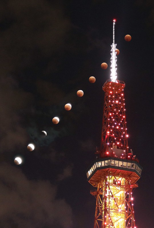 さっぽろテレビ塔の奥で部分月食から皆既月食へと進む満月（午後6時45分から6分間で撮影した10枚を合成）。札幌では午後7時45分ぐらいから月は雲に中に隠れた＝札幌市中央区で2022年11月8日、貝塚太一撮影