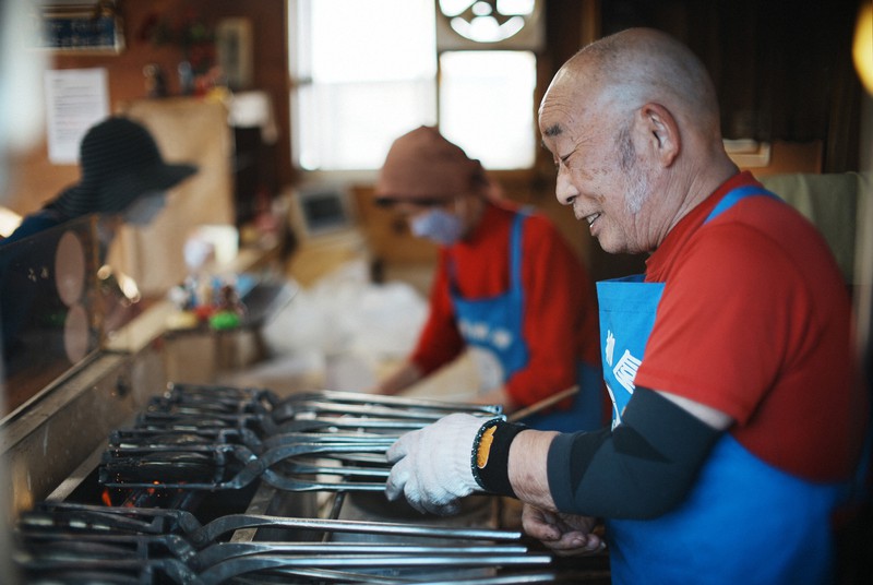 一つ一つ金型に生地とあんを入れ、たい焼きを焼き上げる札幌柳屋の目黒国夫さん(手前)。奥は袋詰めをする妻典子さん=札幌市東区で2022年10月14日、貝塚太一撮影