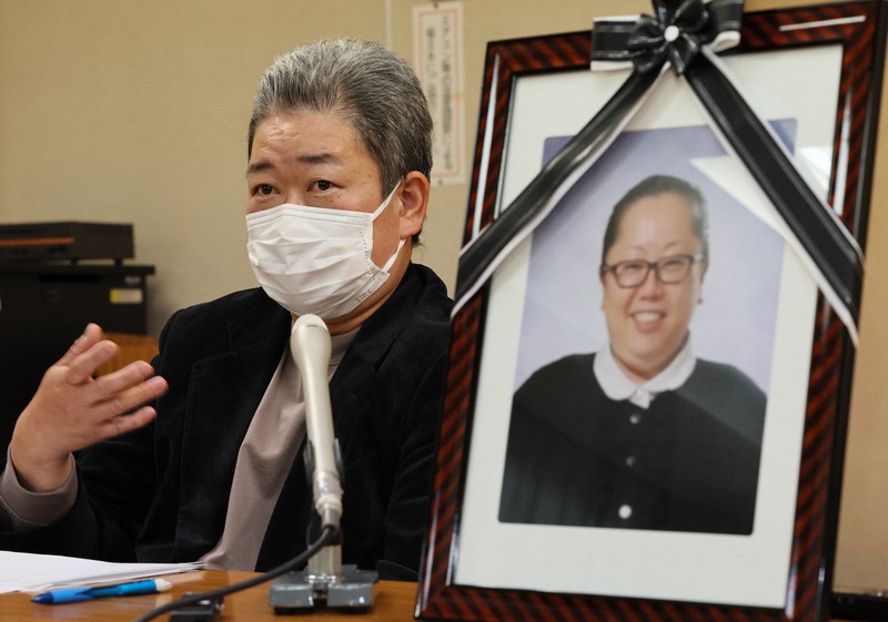 ワクチン接種直後に亡くなった飯岡綾乃さんの遺影を横に記者会見する夫英治さん=愛知県愛西市で2022年11月17日、兵藤公治撮影