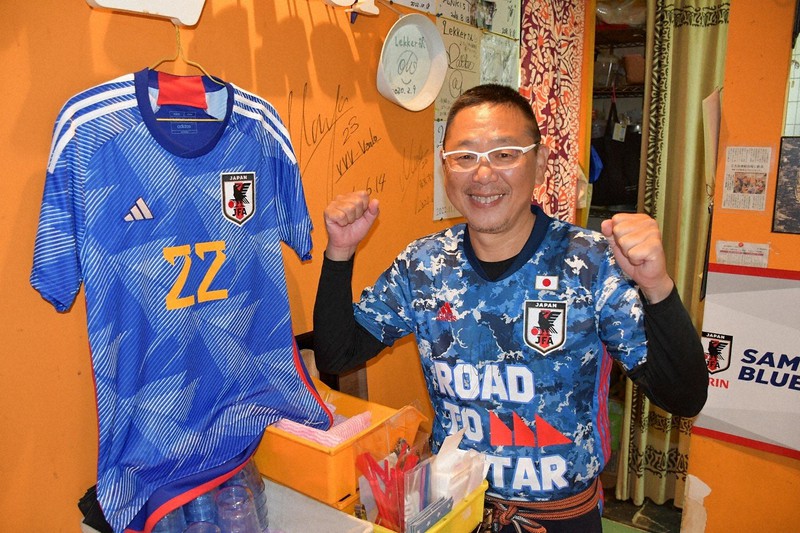 吉田麻也選手の背番号22のユニホームが飾られた店内でエールを送る松島伸一さん=長崎市松が枝町で2022年11月25日午後4時11分、城島勇人撮影