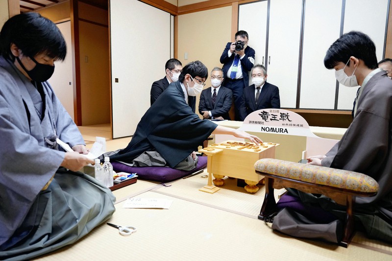 第35期竜王戦七番勝負第6局、封じ手を指す広瀬章人八段(中央)と藤井聡太竜王(右)。左は立会人の藤井猛九段=鹿児島県指宿市の「指宿白水館」で2022年12月3日午前9時(代表撮影)