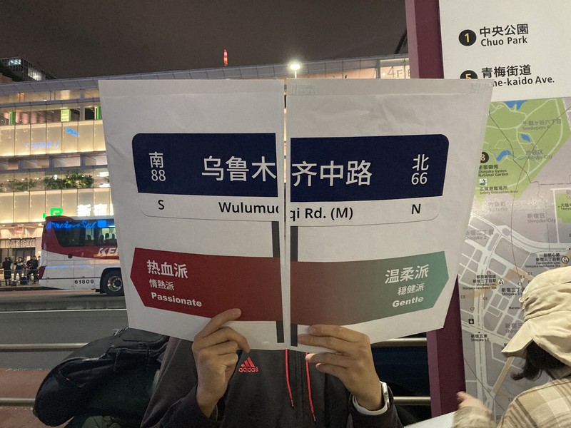 中国のゼロコロナ政策に抗議するデモで、共産党批判などの「情熱派」と火災被害者を弔う「穏健派」に分けたことを示す案内板を持ったスタッフ＝東京都新宿区で11月30日午後8時25分、林哲平撮影