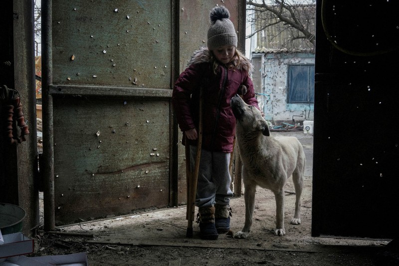 ロシアの侵攻が続く中、兵器によって穴が開いた扉の近くで犬をなでるウクライナの6歳の少女=南部ヘルソン州で2022年12月7日、ロイター