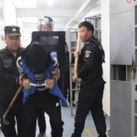 新疆ウイグル自治区の収容施設で、手錠、足かせ、覆面をつけられ監房から連れ出される収容者＝新疆公安ファイルより