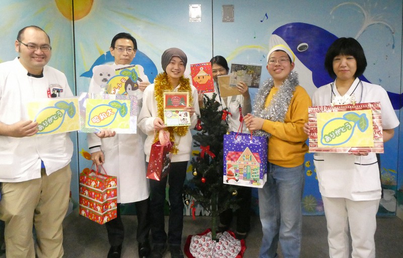 入院闘病中の子どもたちへのクリスマスプレゼントを病院のスタッフに託す「みんレモサンタ」の栄島四郎さん(右から2人目)と亀山晴生さん(同4人目)=昭和大学病院提供
