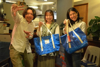 熊本から福島・相馬に広まったブルーシードバッグを手にする高橋あゆみさん（中央）と佐藤かつあきさん（左）＝東京都港区赤坂3のトレジオンポートで2023年4月28日、錦織祐一撮影