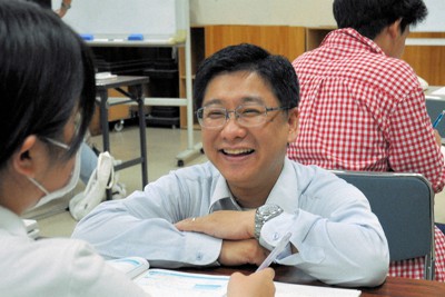 しゃがみ込んで笑顔で生徒に話しかける小宮位之さん（中央）＝東京都八王子市で2023年5月22日、桐野耕一撮影