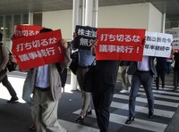 スルガ銀行の株主総会終了後、抗議のプラカードを掲げて会場を後にする株主ら＝静岡県沼津市で6月29日午後0時半、今沢真撮影