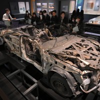 津波に襲われて殉職した佐藤雄太さんら2人の警察官が乗っていたパトカーの前で説明を聞く高校生ら＝福島県富岡町のとみおかアーカイブ・ミュージアムで2024年2月1日、手塚耕一郎撮影