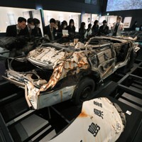 津波に襲われて殉職した佐藤雄太さんら2人の警察官が乗っていたパトカーの前で説明を聞く高校生ら＝福島県富岡町のとみおかアーカイブミュージアムで2024年2月1日、手塚耕一郎撮影