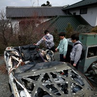 津波にの襲われて大破し、自動車整備工場に保管中のパトカーに触れる富岡町の職員ら。展示を前に保存処理が行われた＝福島県の同町で2015年2月25日、森田剛史撮影